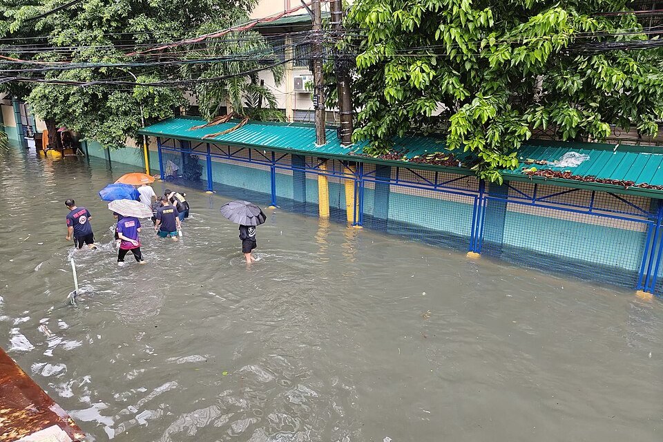 Pedestrians carrying umbrellas while wading through a flooded street in Quiapo, Manila, during heavy monsoon rains