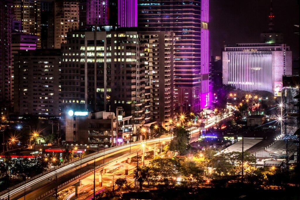 Ortigas Center skyline at night with illuminated high-rise buildings, purple lighting and traffic trails along an elevated road