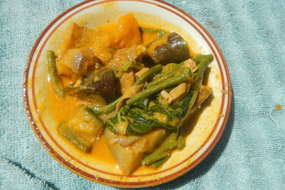 Plate of Filipino kare-kare stew with eggplant, green beans and leafy vegetables in a rich orange sauce