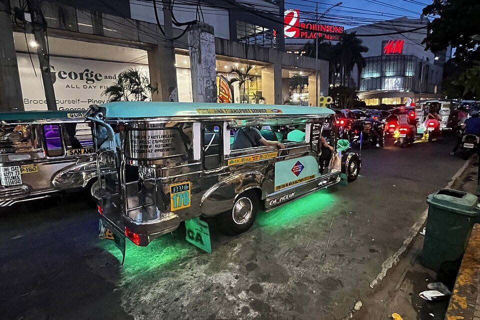 Traditional silver jeepney with green lighting on a busy Manila street near Robinsons Place Manila at dusk