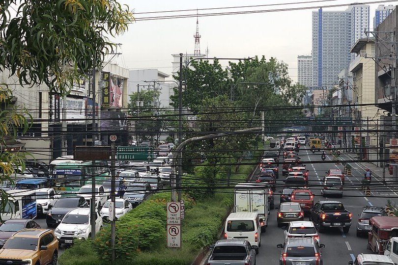 Heavy traffic on Quezon Avenue in Metro Manila, with cars, buses and jeepneys beneath overhead utility cables
