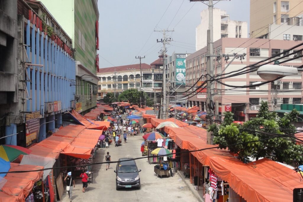 Busy shopping district along C.M. Recto Avenue in Divisoria, Manila
with orange market stalls, colourful umbrellas, pedestrians and vehicles