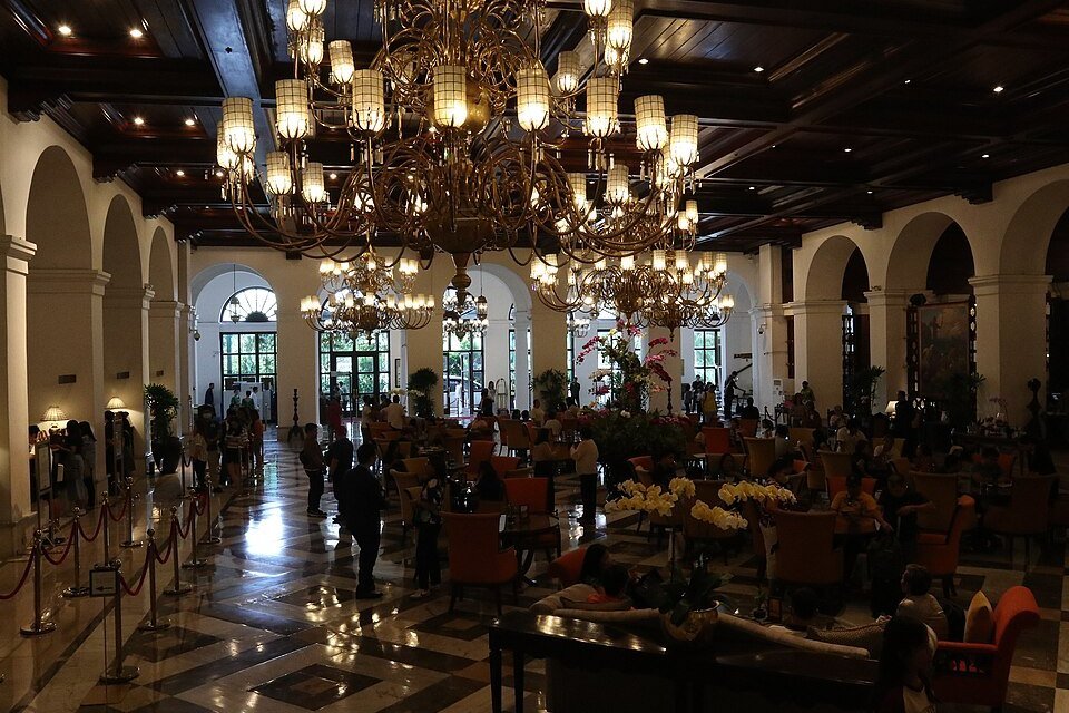 Elegant lobby of the Manila Hotel with large chandeliers, arched windows, polished marble floors and seating areas