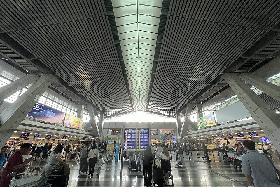 Departure hall at NAIA Terminal 3 in Manila, showing airline check-in counters, flight information screens and travelers with luggage