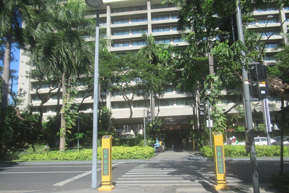 Street entrance to The Peninsula Manila hotel in Makati, with palm trees, landscaped grounds and a pedestrian crossing