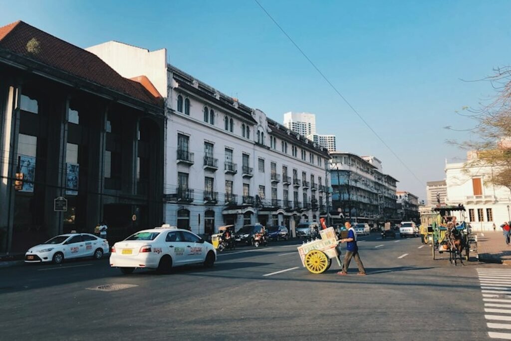 Historic street in Manila with colonial-era buildings, taxis, a horse-drawn carriage and a street vendor