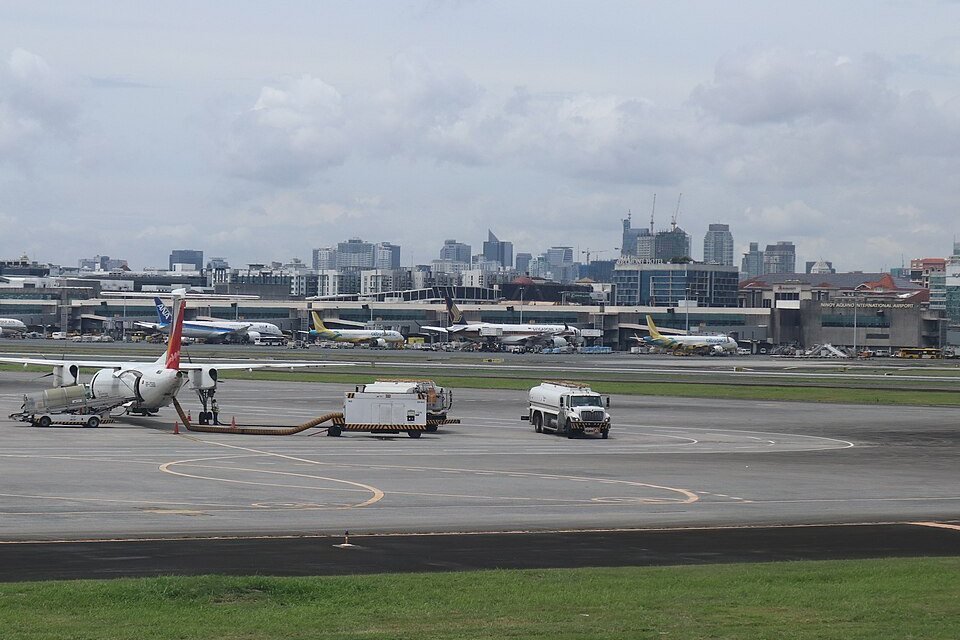 Aircraft parked near the terminals at Ninoy Aquino International Airport in Manila, with service vehicles and the city skyline behind