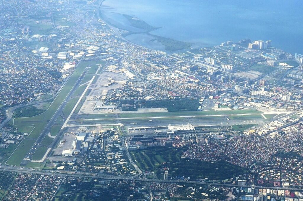 Aerial view of Ninoy Aquino International Airport showing intersecting runways, terminal buildings and surrounding Manila neighborhoods