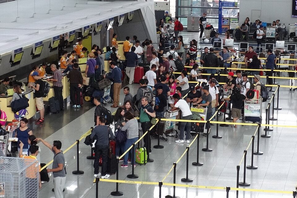 Travelers with luggage queuing at airline check-in counters inside NAIA Terminal 3 in Manila