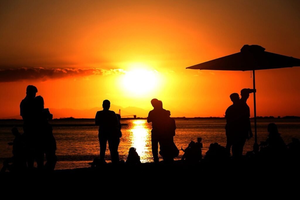 People relaxing beside Manila Bay as the sun sets over the water