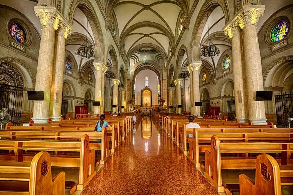 Interior of Manila Cathedral with wooden pews, tall stone columns, vaulted ceilings and the altar