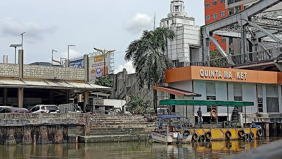 Quinta Market building beside a waterway in Quiapo, Manila, with small boats and a pedestrian bridge