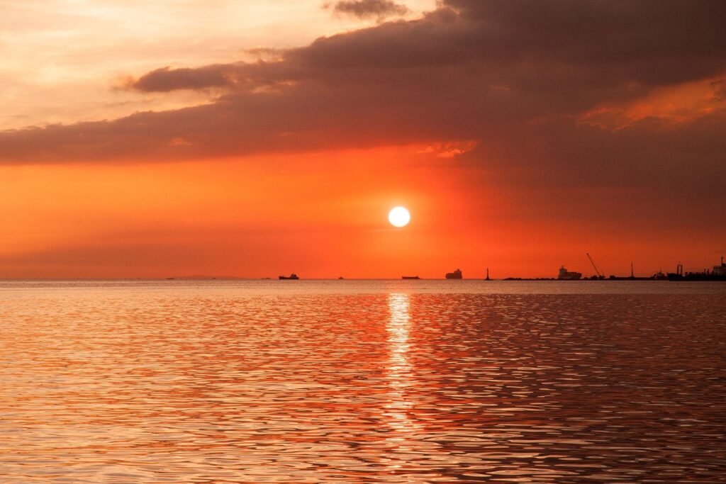 Bright orange sunset over Manila Bay, with the sun reflecting on the water and ships along the horizon