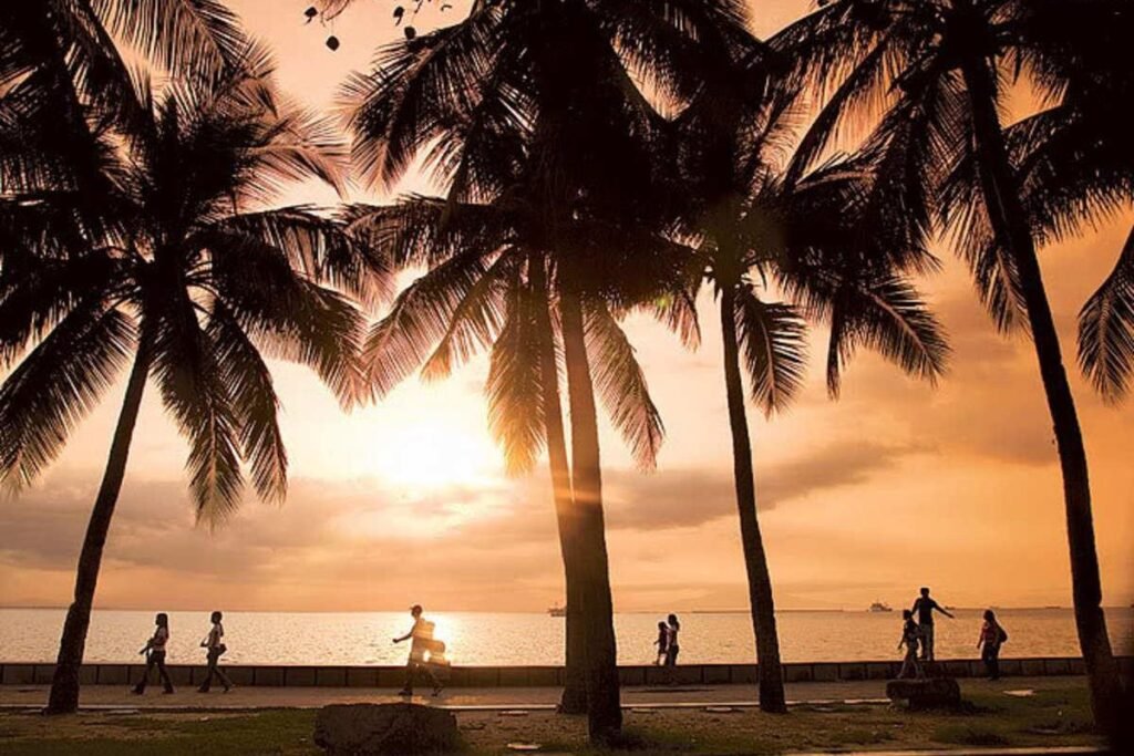Silhouetted palm trees and people walking along Manila Baywalk during a golden sunset