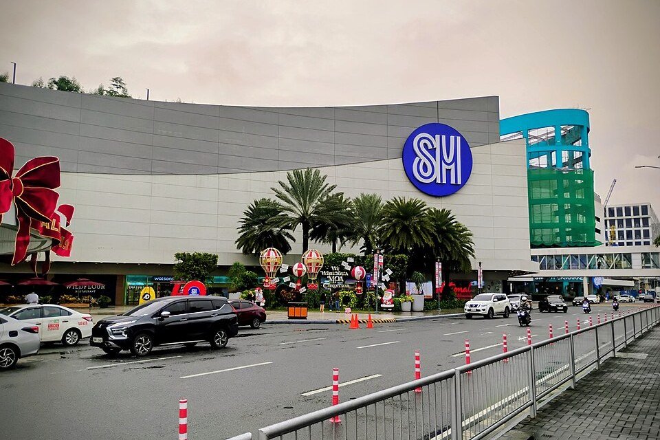Exterior of SM Mall of Asia in Pasay, with its large blue SM logo, palm trees and traffic along the road