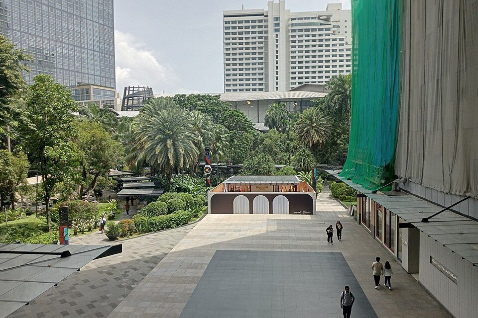 Open-air pedestrian plaza at Greenbelt in Makati, with landscaped gardens, palm trees and surrounding buildings