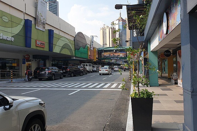 Street outside Greenhills Shopping Center with parked cars, shops and a pedestrian crossing