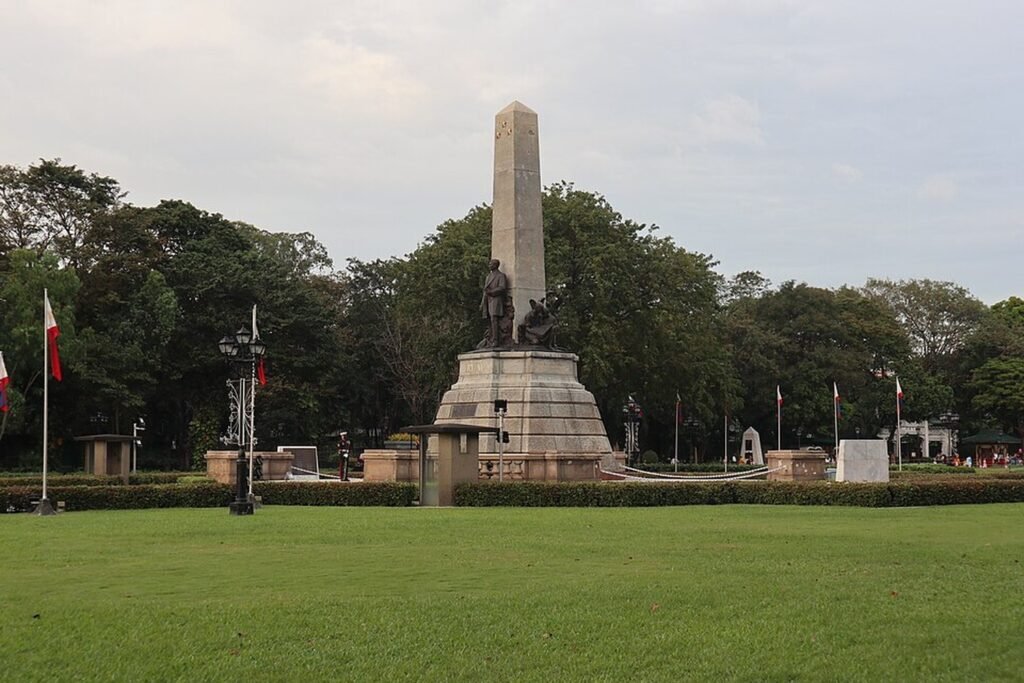 Rizal Monument surrounded by green lawns, trees and Philippine flags at Rizal Park in Manila