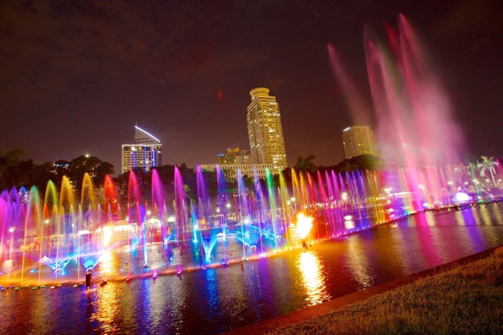 Colourful illuminated fountains at Rizal Park in Manila, with city buildings in the background at night