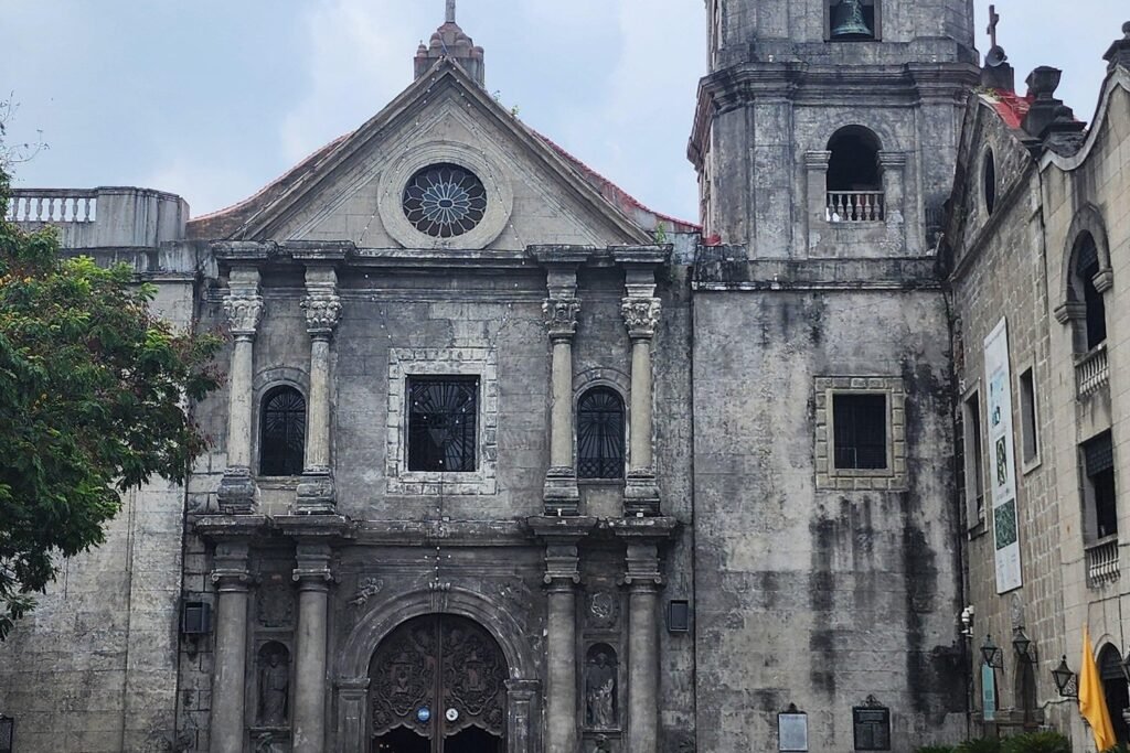 Stone facade of San Agustin Church in Intramuros, Manila, showing its carved entrance, circular window and bell tower