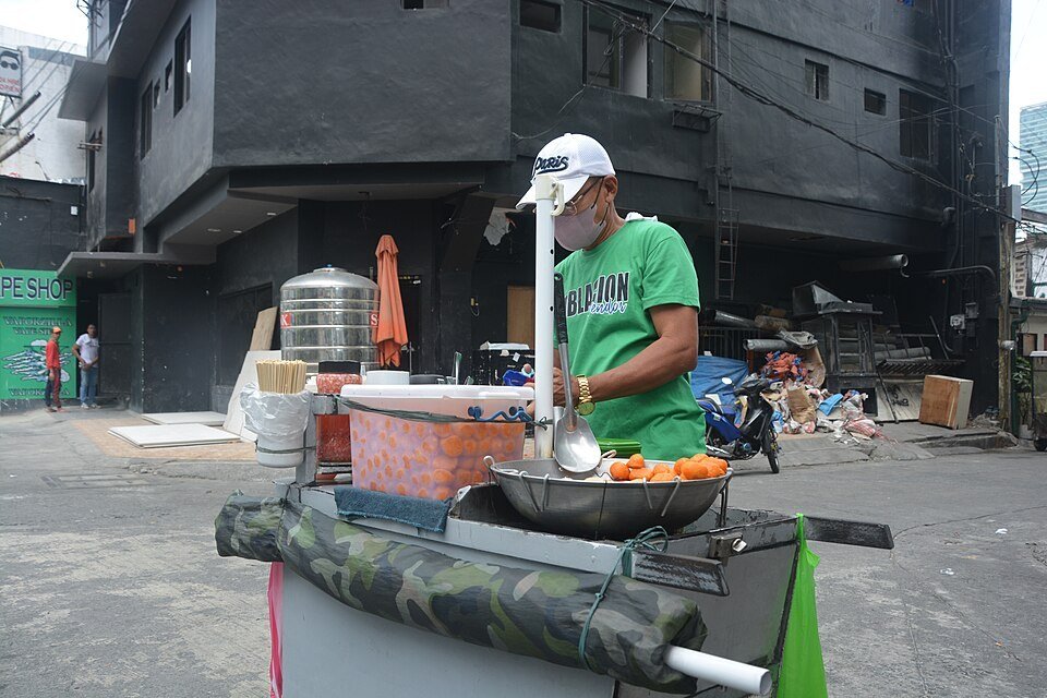 Street food vendor in a green shirt preparing food at a roadside cart in Manila