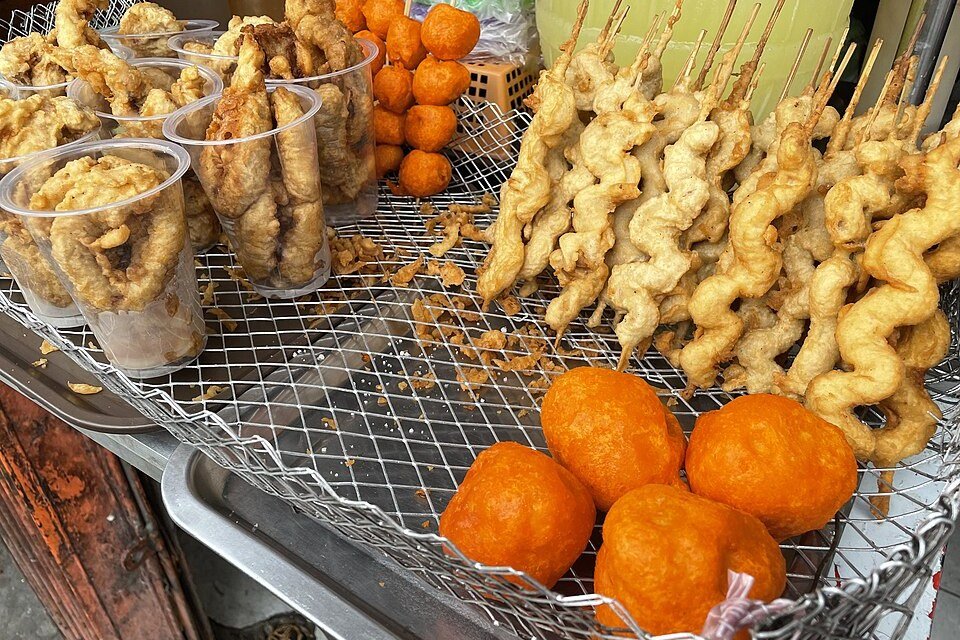 Filipino street food stall displaying orange fried balls, battered skewers and fried snacks in plastic cups