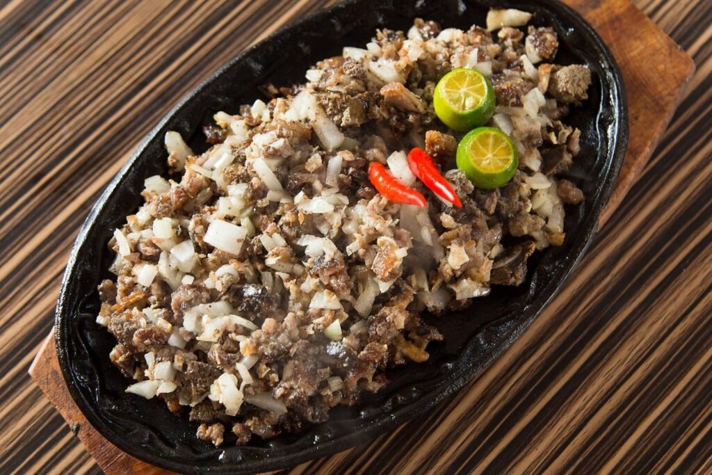 Filipino sizzling sisig served on a hot iron plate with chopped onions, red chillies and calamansi