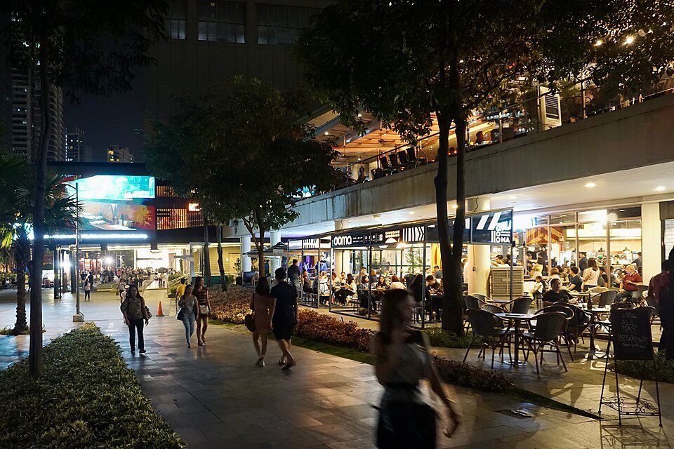 Outdoor restaurants and cafés with diners and pedestrians along a brightly lit walkway in BGC at night